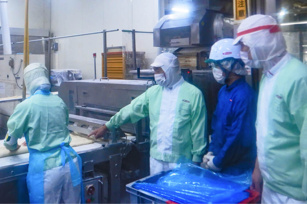 工場内で改善活動の指導を行う作業員たち。食品製造の安全性と品質向上を目指した取り組みの様子。
